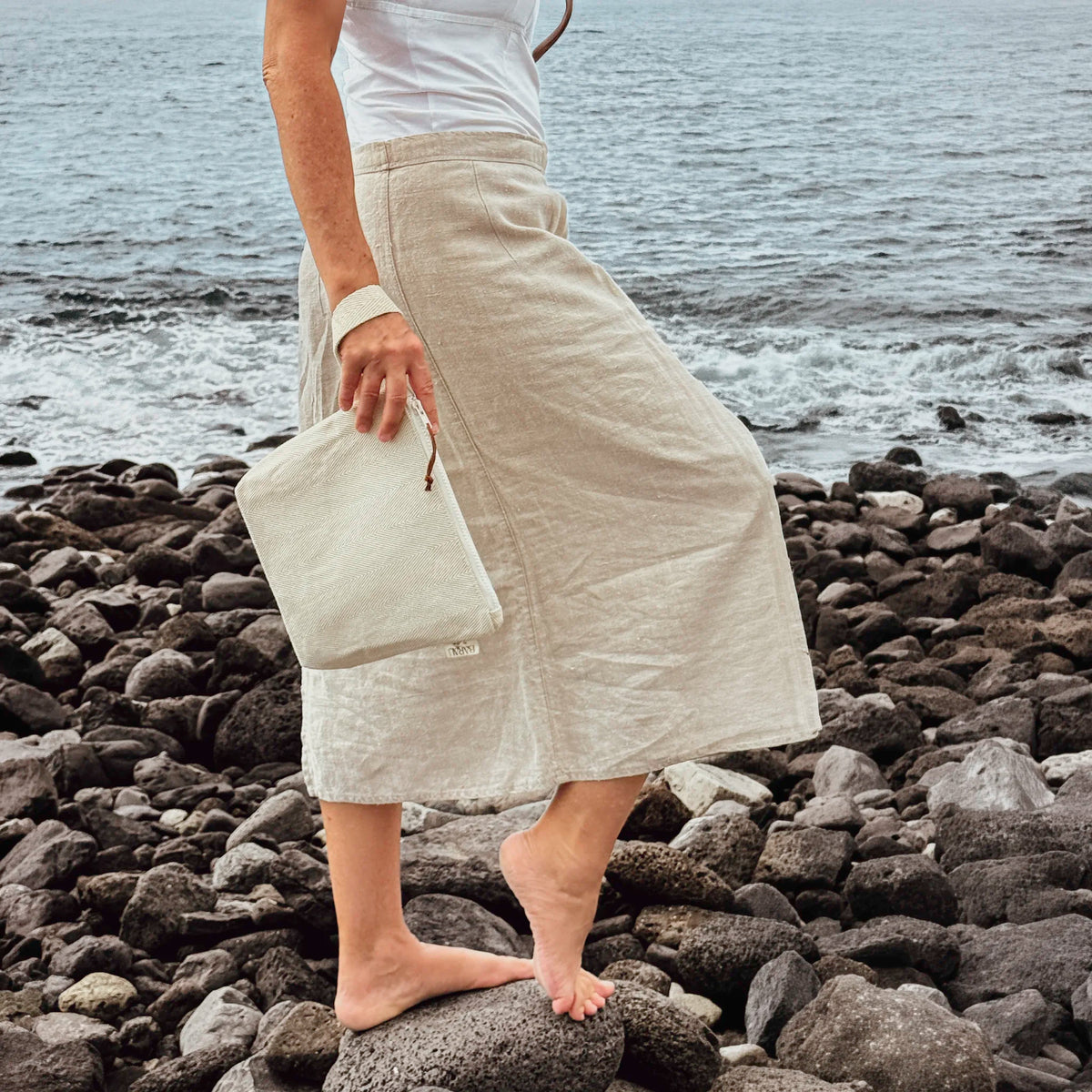Woman carrying the BARAU Carry the Calm cosmetic bag on a pebble beach